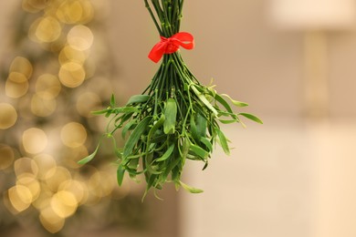 Photo of Mistletoe bunch with red bow on blurred background, bokeh effect. Traditional Christmas decor