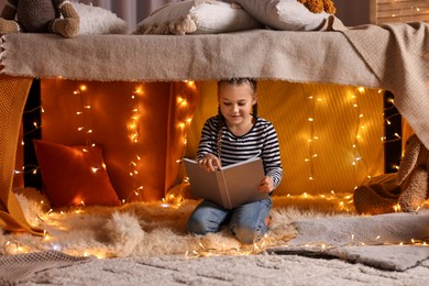 Girl reading book in decorated play tent at home