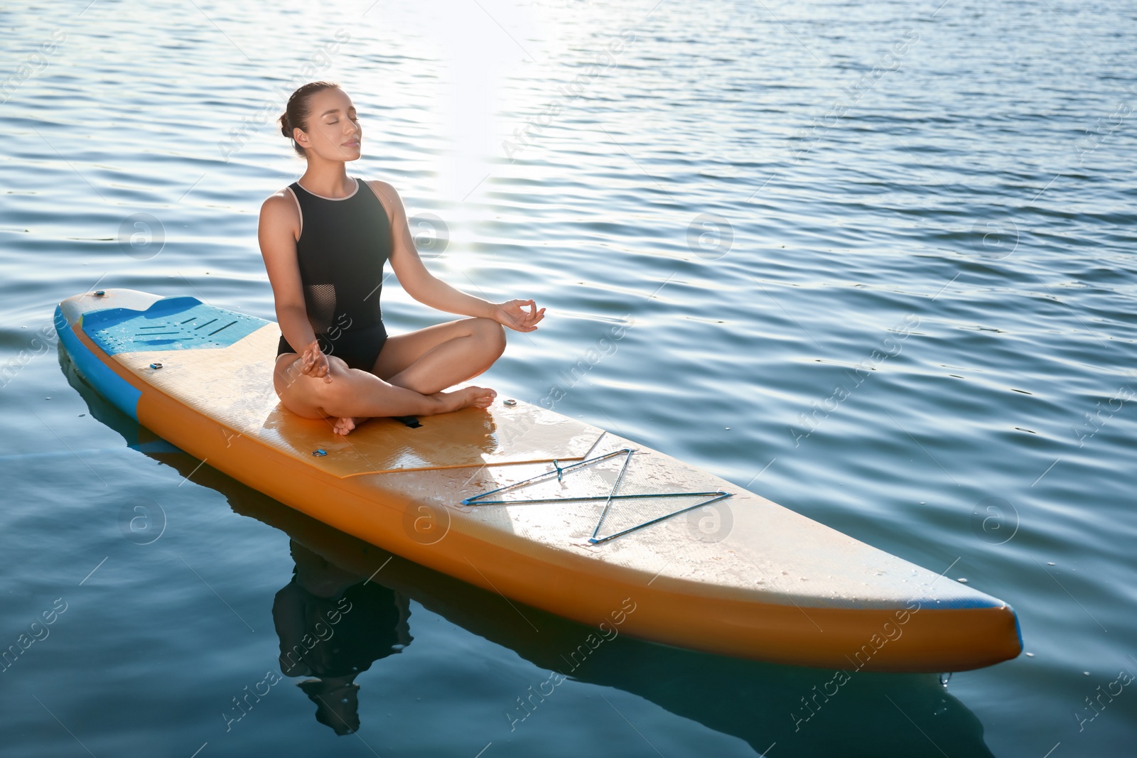 Photo of Young meditating yoga on color SUP board on river at sunset