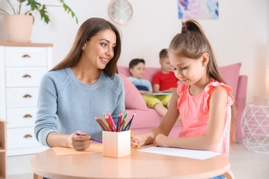 Photo of Cute little child drawing at table with young woman in playing room