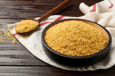 Photo of Bowl and spoon with raw bulgur on wooden table