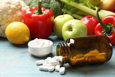 Photo of Dietary supplements. Overturned bottle and bowl with pills near food products on light blue wooden table