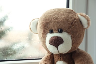 Cute lonely teddy bear on windowsill indoors, closeup