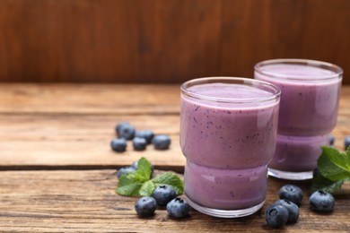 Photo of Glasses of blueberry smoothie with mint and fresh berries on wooden table. Space for text