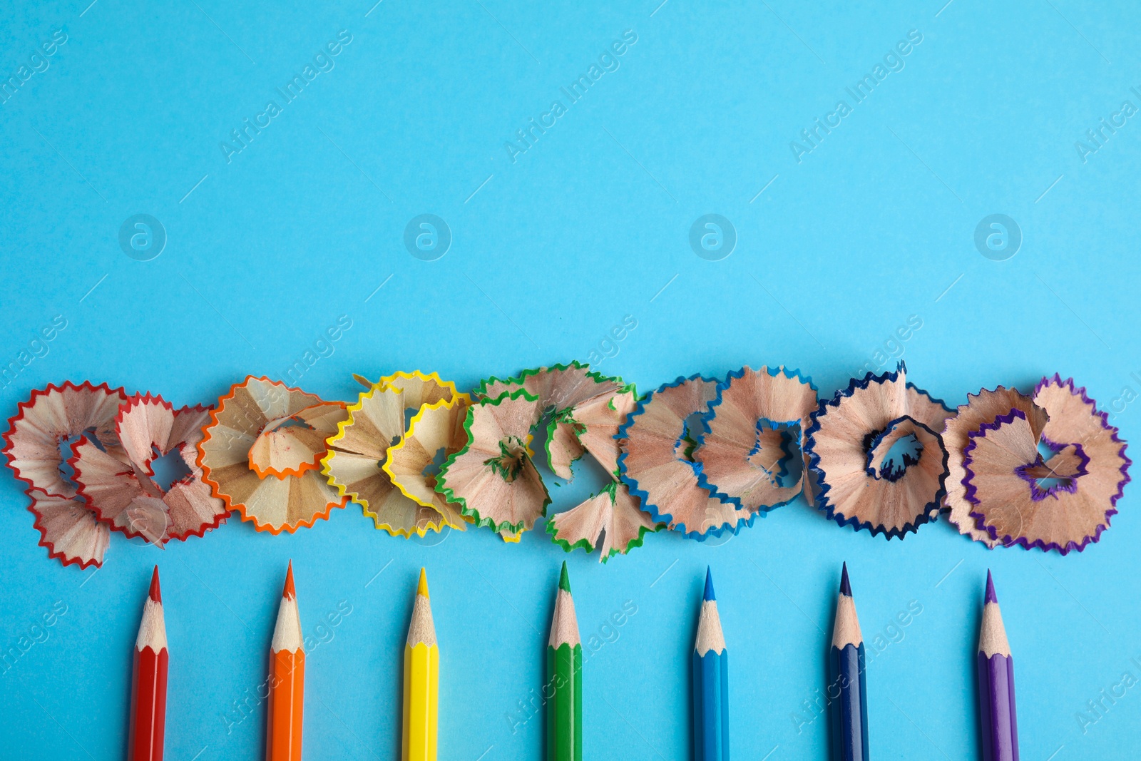 Photo of Color pencils and shavings on blue background, flat lay. Space for text