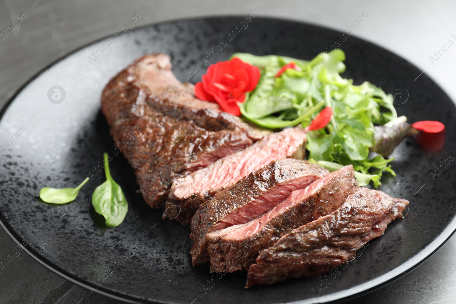 Photo of Pieces of delicious grilled beef meat and greens on table, closeup