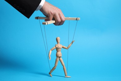 Photo of Man pulling strings of puppet on light blue background, closeup