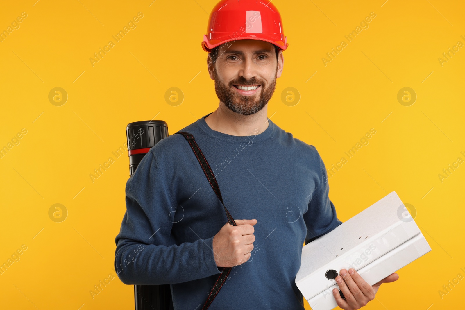Photo of Architect in hard hat with drawing tube and folders on orange background
