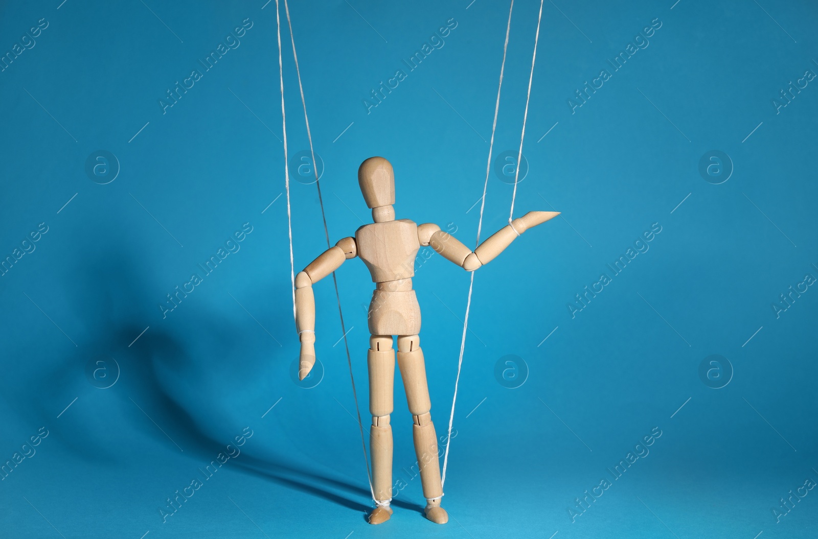 Photo of One wooden puppet with strings on light blue background