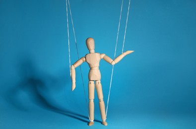 Photo of One wooden puppet with strings on light blue background