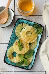 Tasty grilled pineapple slices, honey and wooden spoon on light gray tiled table, flat lay