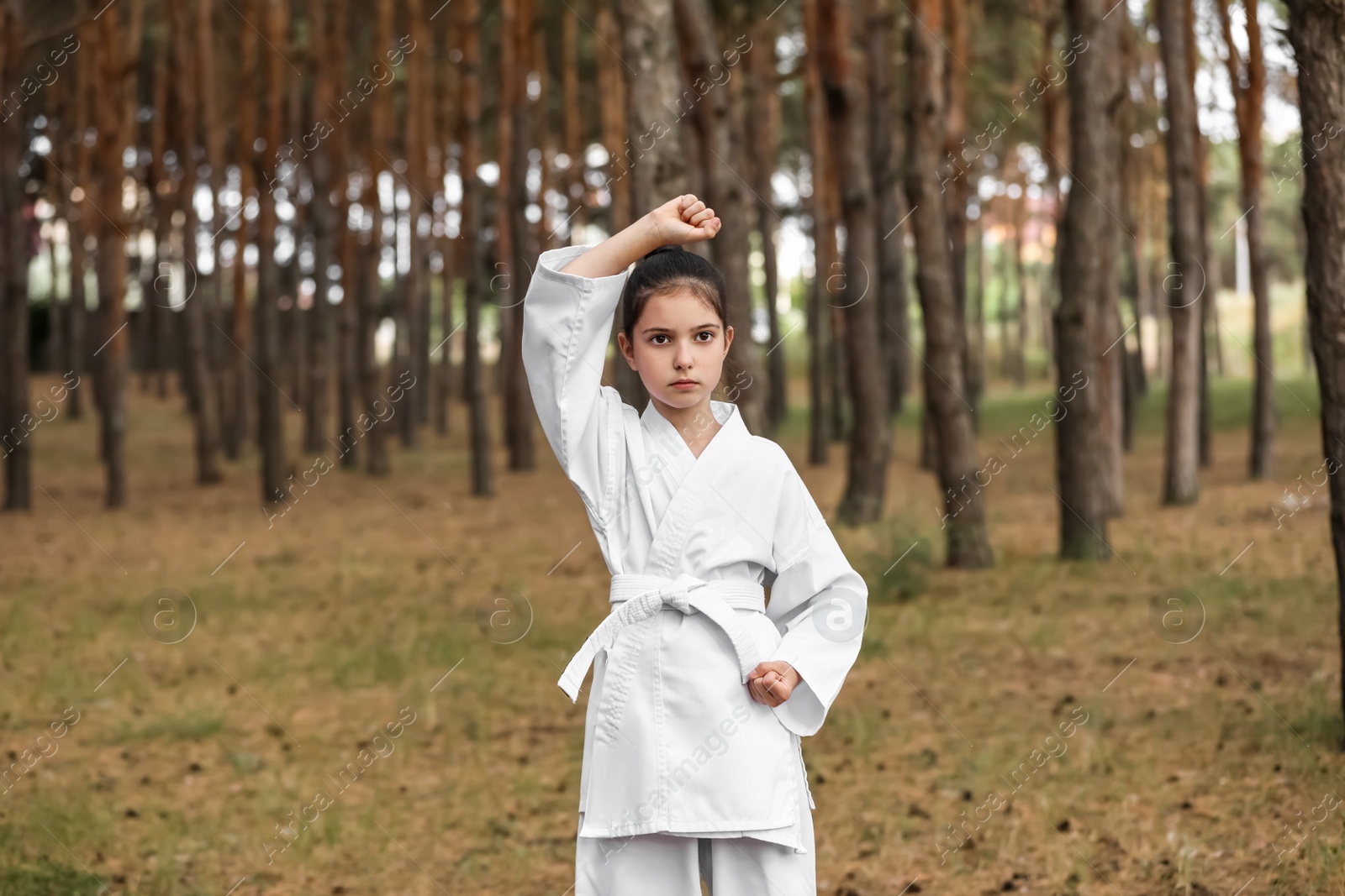 Photo of Cute little girl in kimono practicing karate in forest