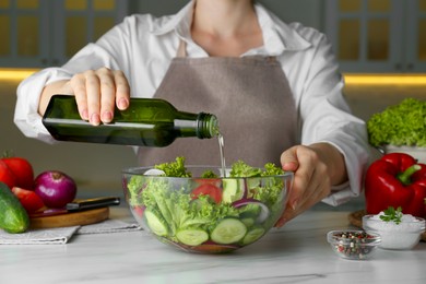 Photo of Woman adding cooking oil to delicious salad at table, closeup