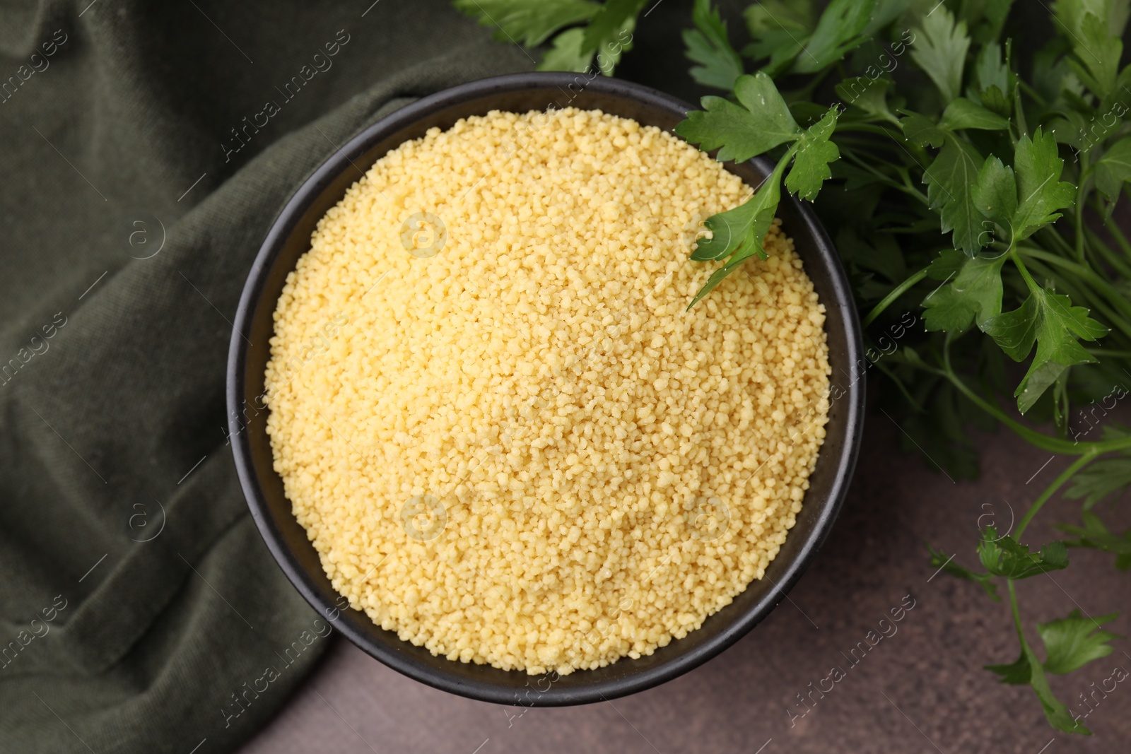 Photo of Raw couscous in bowl and parsley on table, top view