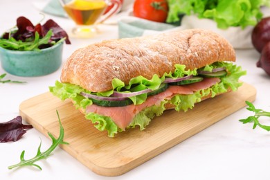 Photo of Delicious sandwich with fresh vegetables and salmon on white table, closeup
