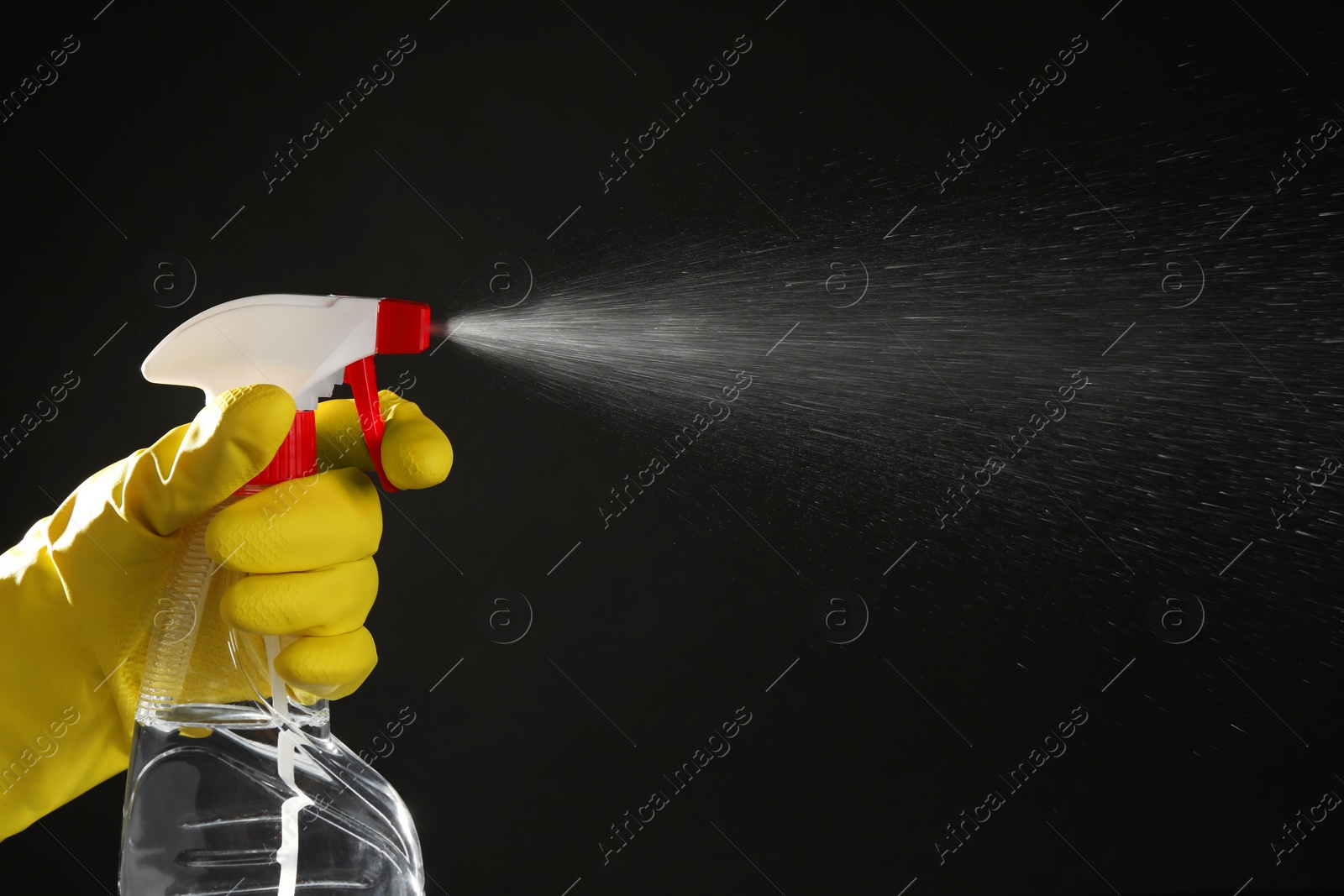 Photo of Woman spraying liquid from bottle on black background, closeup