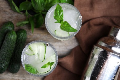 Glasses of refreshing cucumber water with basil on wooden table, flat lay