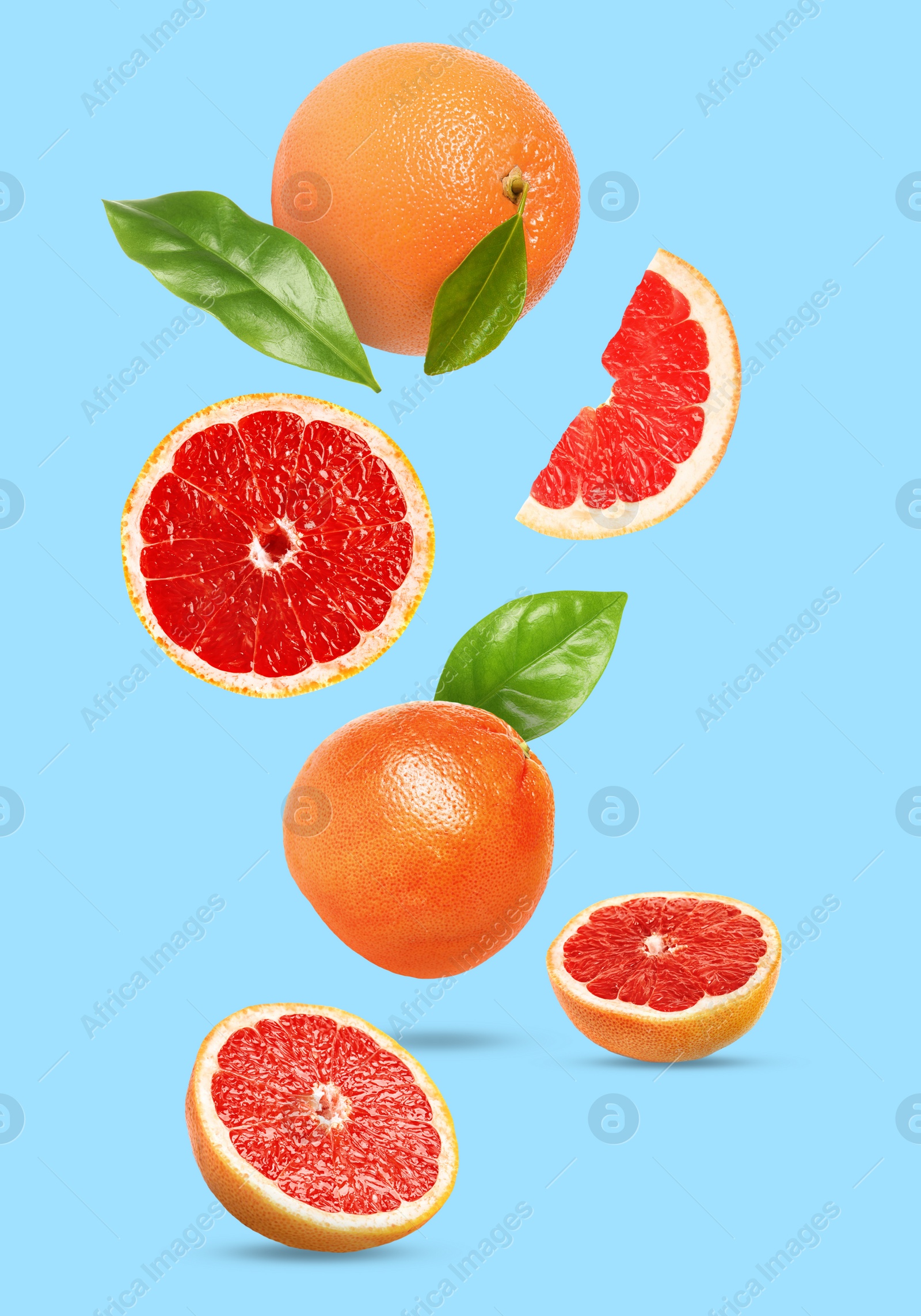 Image of Tasty ripe grapefruits and green leaves falling on light blue background