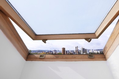 Photo of Beautiful view of cityscape from open skylight roof window on slanted ceiling. Attic room