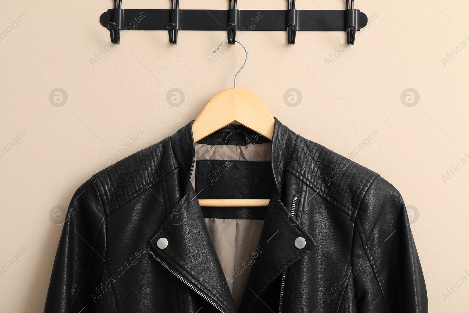 Photo of Hanger with black leather jacket on beige wall