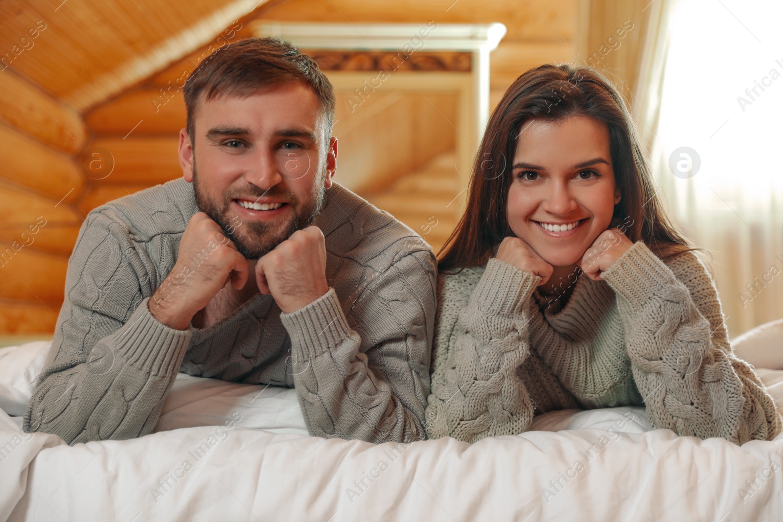 Photo of Young couple wearing warm sweaters on bed at home