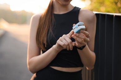 Photo of Woman checking pulse with blood pressure monitor on finger after training outdoors, closeup