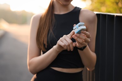 Woman checking pulse with blood pressure monitor on finger after training outdoors, closeup