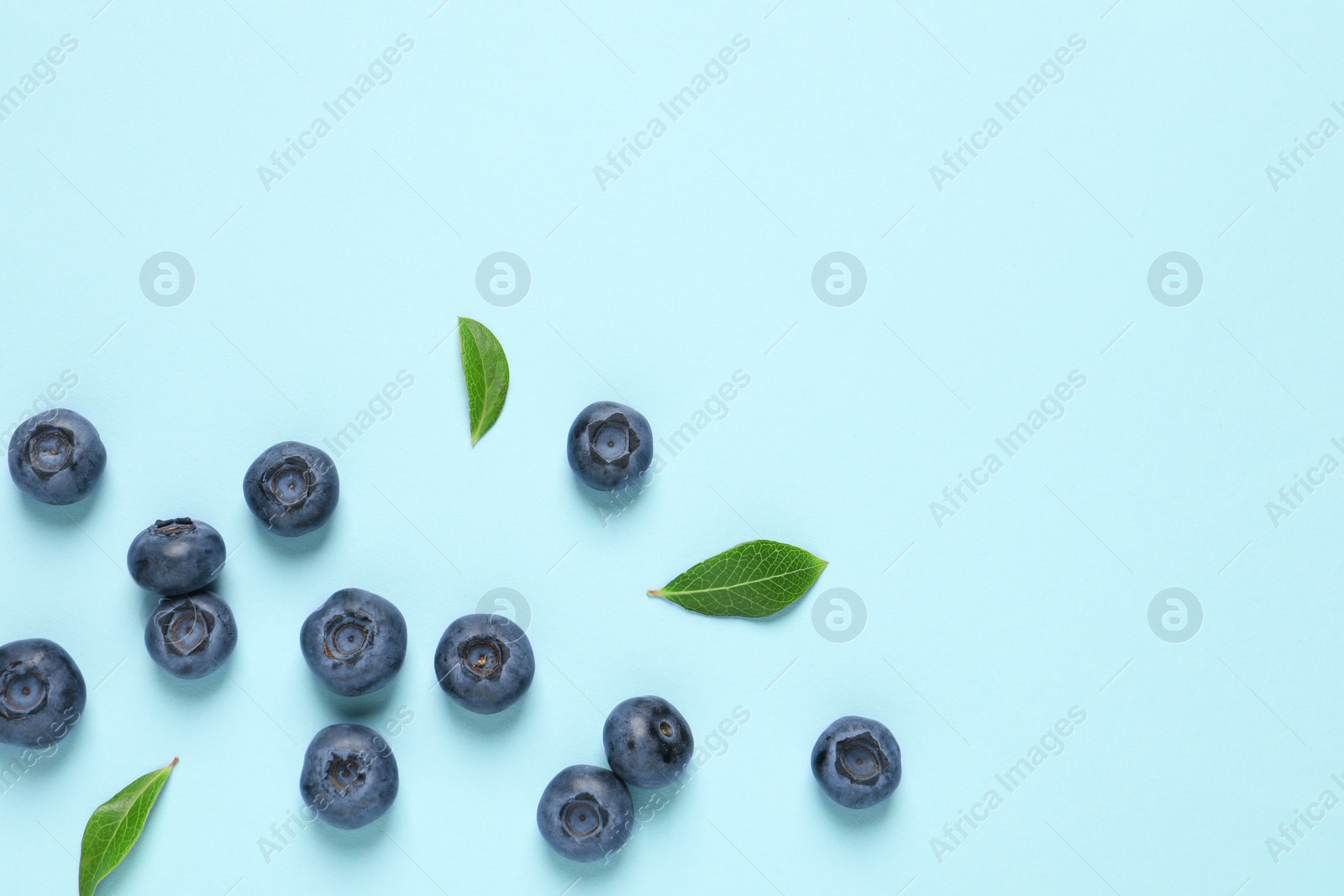 Photo of Tasty fresh blueberries with green leaves on light blue background, flat lay. Space for text