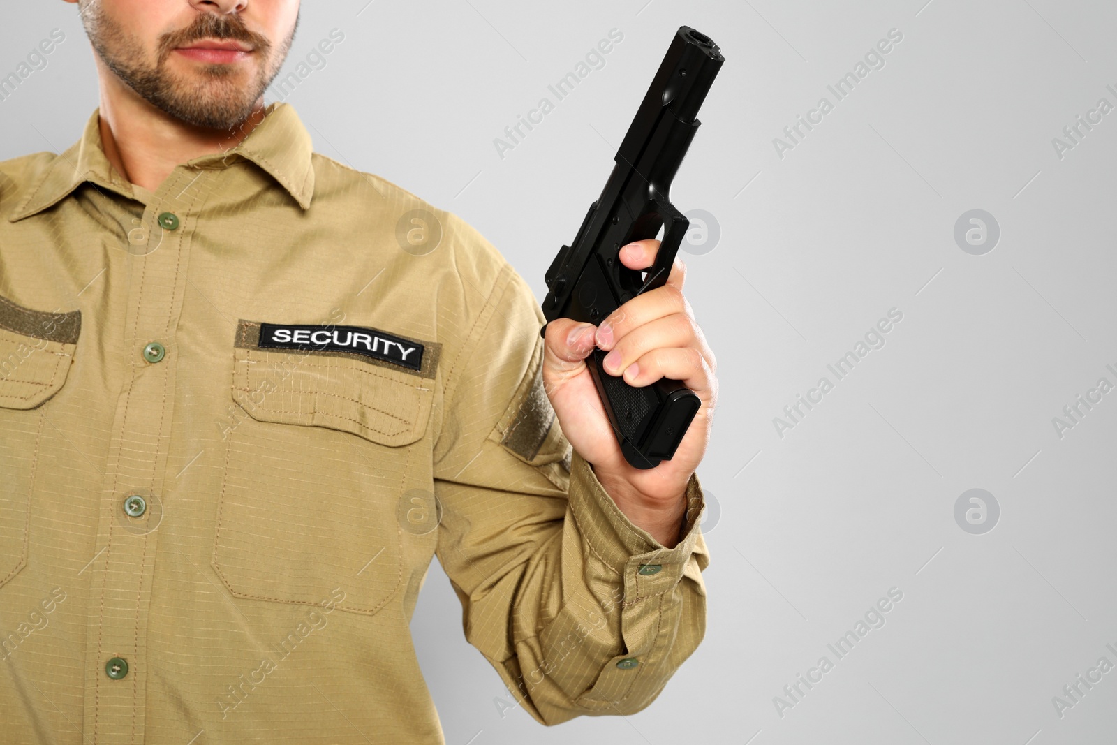 Photo of Male security guard in uniform with gun on grey background, closeup. Space for text