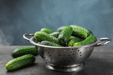 Photo of Colander with ripe fresh cucumbers on table