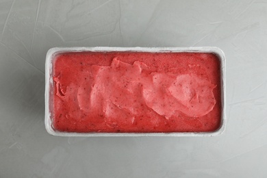 Photo of Container with delicious pink ice cream on grey table, top view
