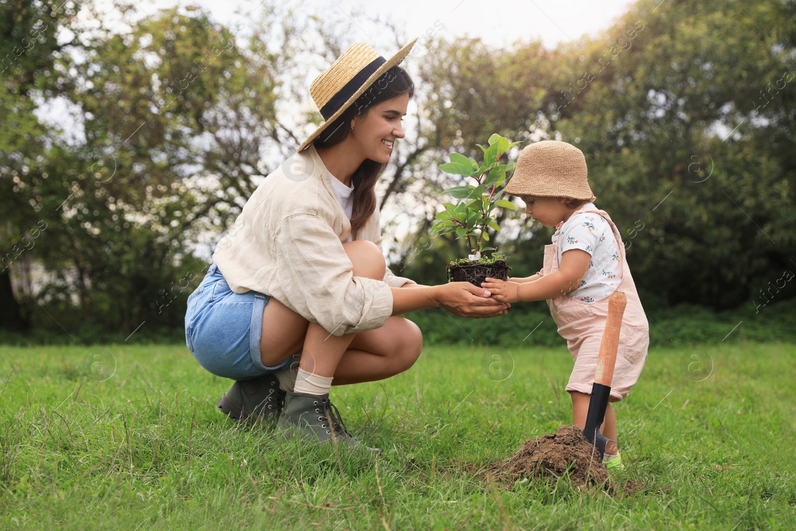 Photo of Mother and her baby daughter planting tree together in garden