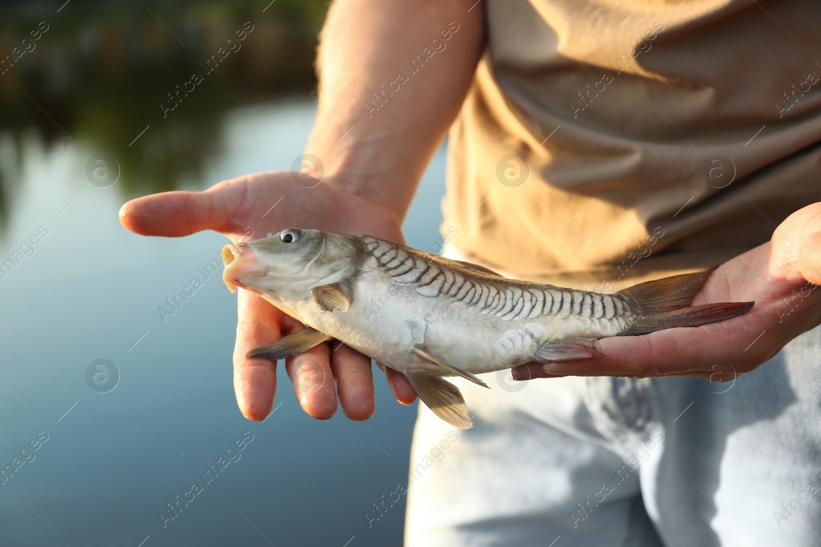 Photo of Man holding caught fish at lake, closeup