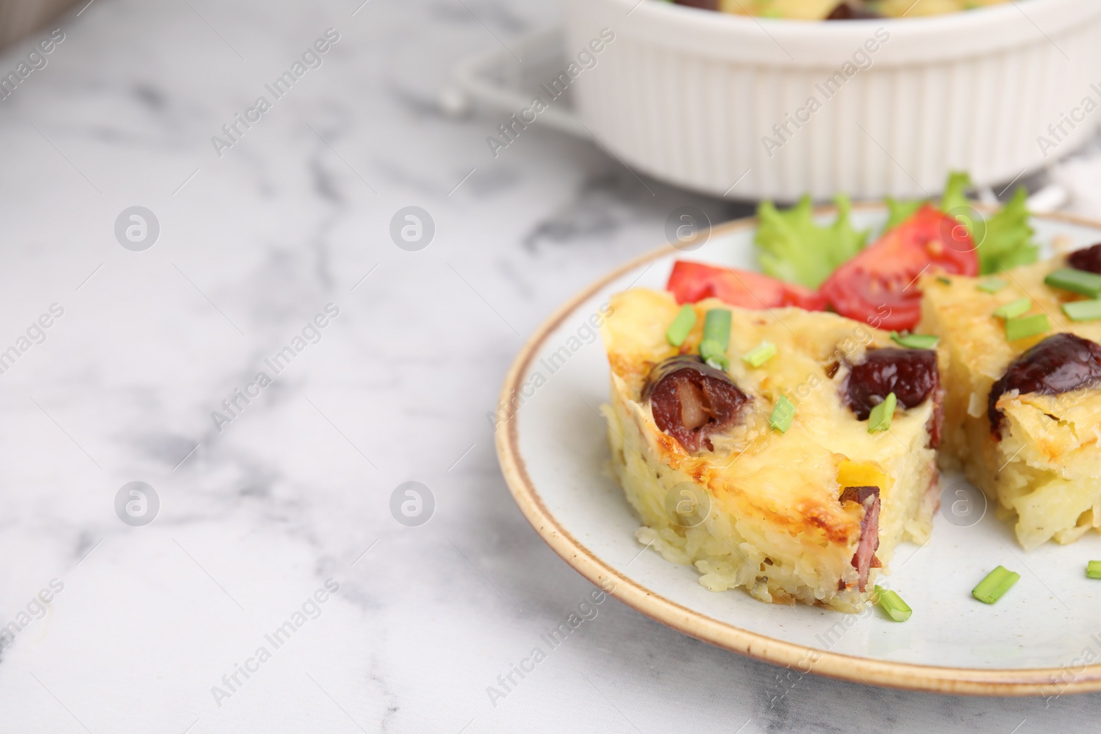 Photo of Tasty sausage casserole with green onions and vegetables served on white marble table, closeup. Space for text