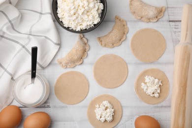 Photo of Process of making dumplings (varenyky) with cottage cheese. Raw dough and ingredients on white wooden table, flat lay