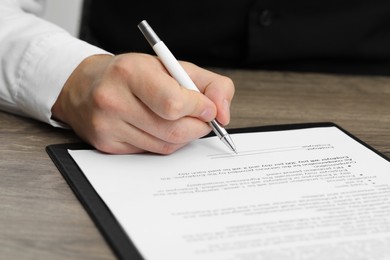 Photo of Man signing document at wooden table, closeup