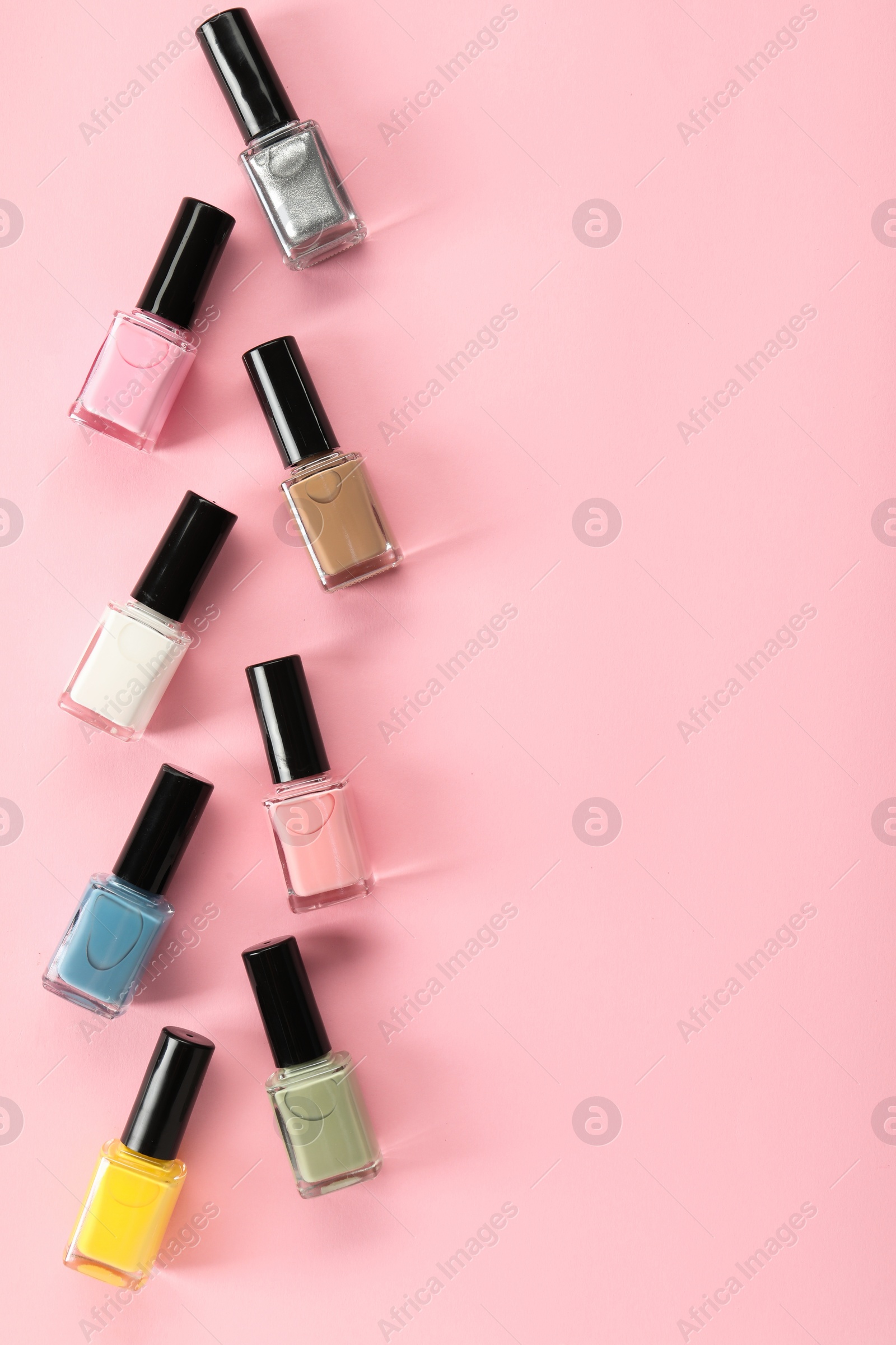 Photo of Pastel nail polishes in bottles on pink background, flat lay. Space for text