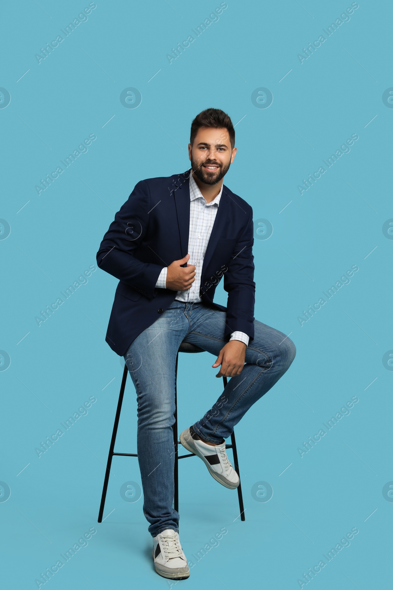 Photo of Handsome young man sitting on stool against turquoise background