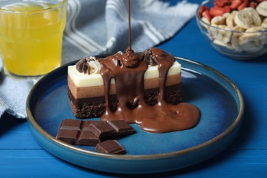 Photo of Pouring chocolate onto tasty mousse cake at blue wooden table