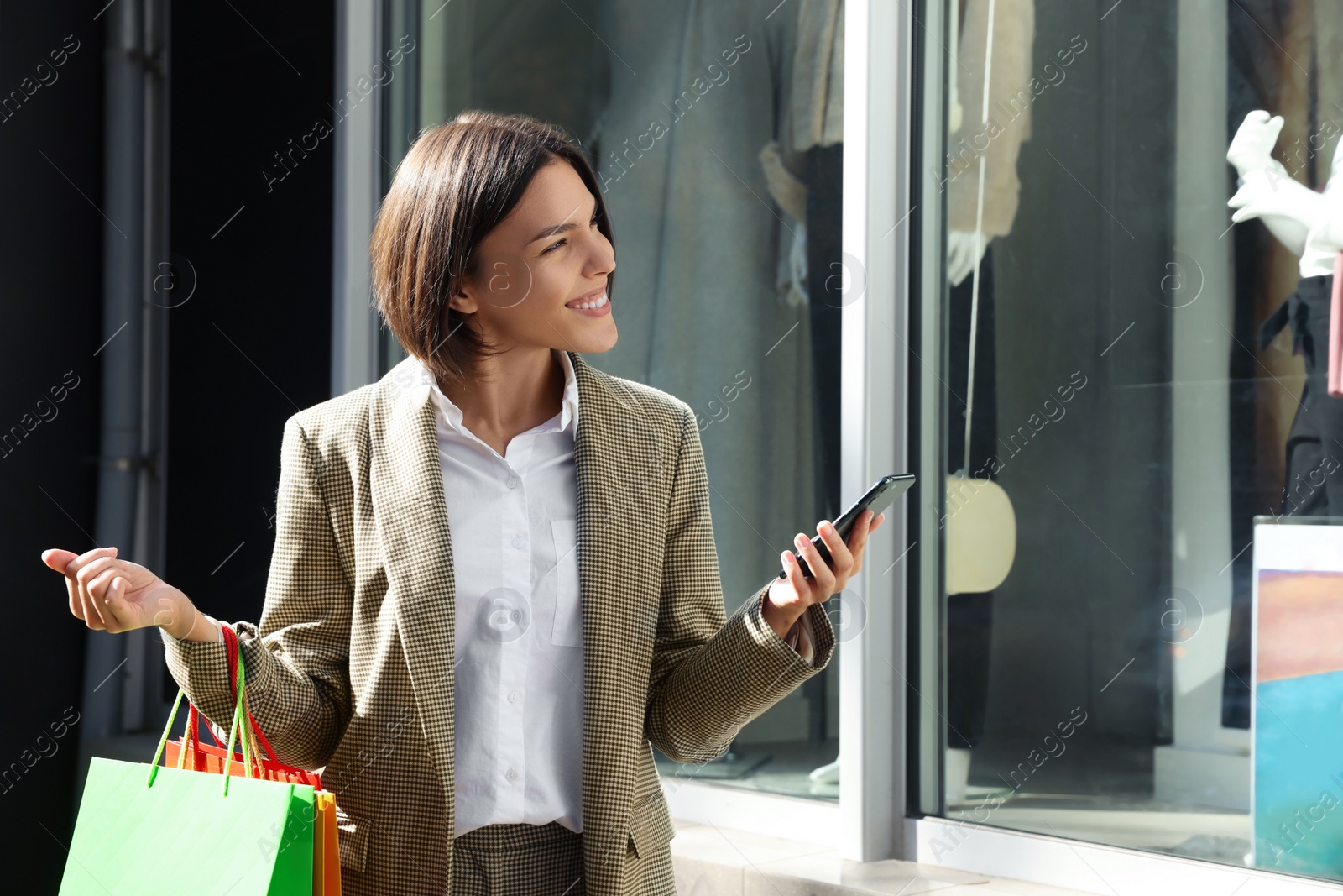 Photo of Special Promotion. Happy young woman with shopping bags and smartphone on city street