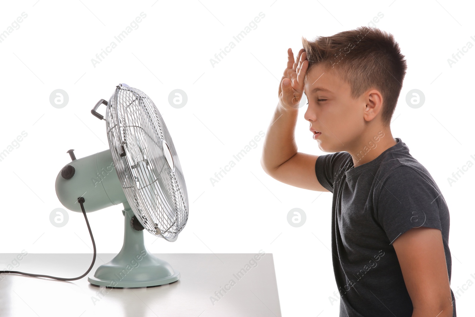 Photo of Little boy suffering from heat in front of fan on white background. Summer season