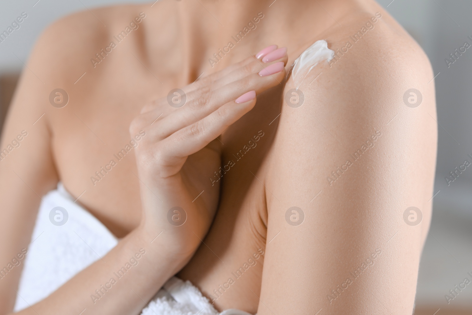 Photo of Woman applying body cream onto shoulder on blurred background, closeup