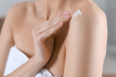 Woman applying body cream onto shoulder on blurred background, closeup