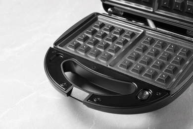 Photo of Modern waffle iron on grey marble table, closeup