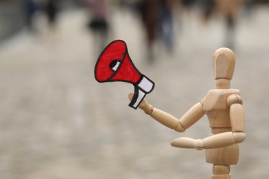 Wooden human figure with paper megaphone on city street, closeup. Space for text