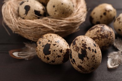 Photo of Quail eggs and feathers near nest on wooden table, closeup