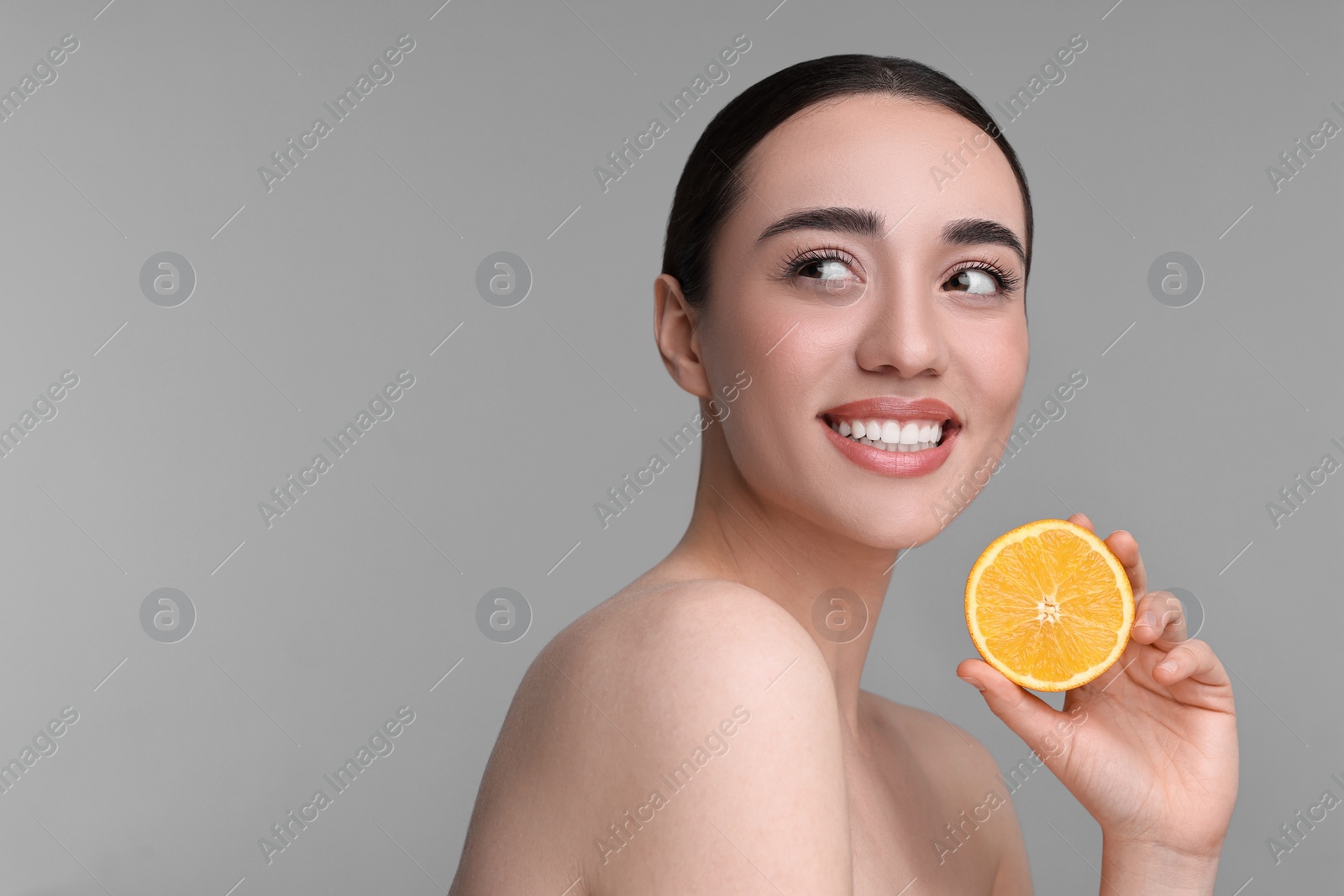 Photo of Beautiful young woman with piece of orange on grey background. Space for text