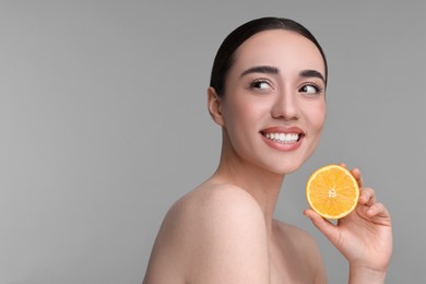 Photo of Beautiful young woman with piece of orange on grey background. Space for text