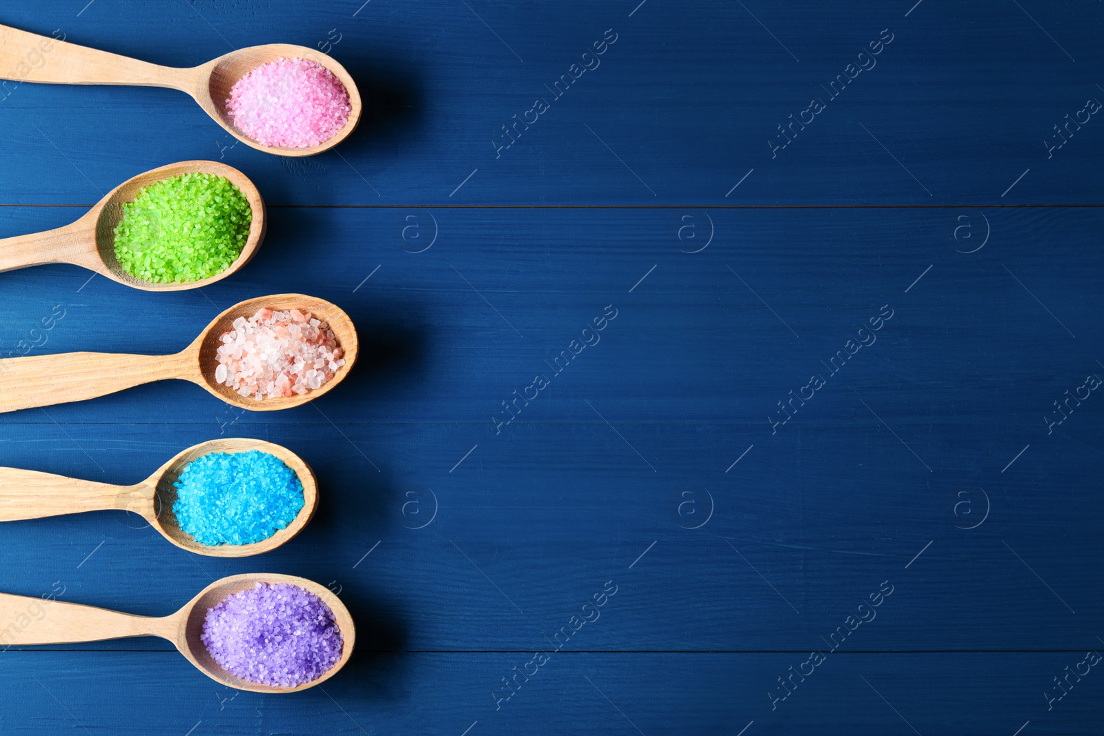 Photo of Spoons with colorful sea salt on blue wooden table, flat lay. Space for text