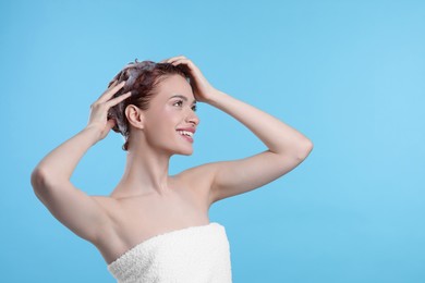 Happy young woman washing her hair with shampoo on light blue background, space for text